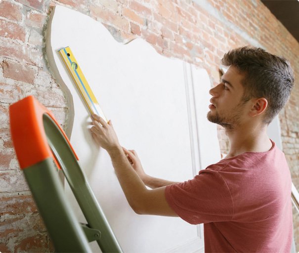 Handyman measuring and aligning drywall on a brick wall using a spirit level