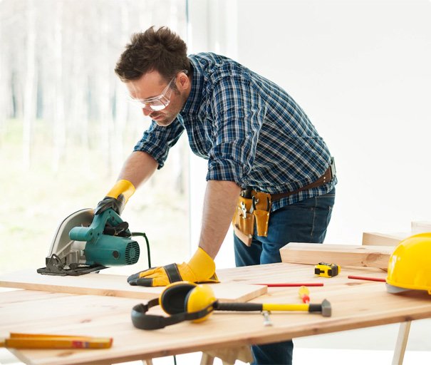 Carpenter cutting wooden boards with a circular saw on a workbench.