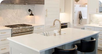 Modern white kitchen with island sink, marble backsplash, and stainless steel appliances.