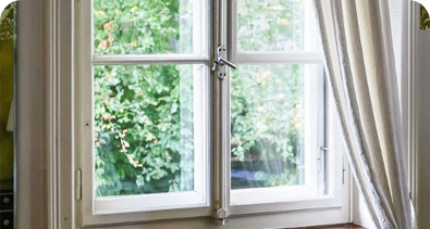 White-framed window with open curtains overlooking a lush green garden.