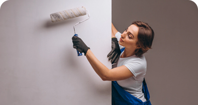 Female painter using a roller to paint a wall white while wearing gloves and overalls.