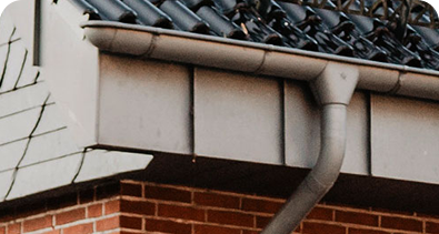 Close-up of a house roof with metal guttering and downpipe attached to a brick wall