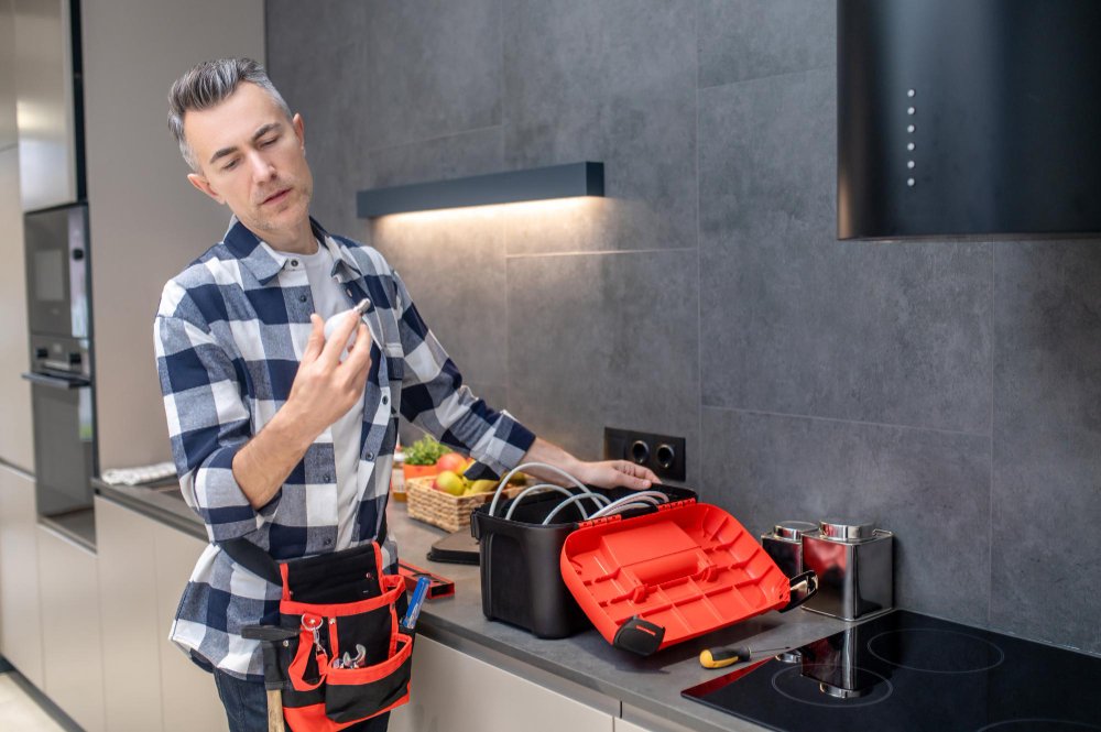 Electrician inspecting a light bulb while working in a modern kitchen with a toolbox on the counter.